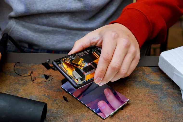 A technician lifting a cracked display away from a phone chassis on the repair bench
