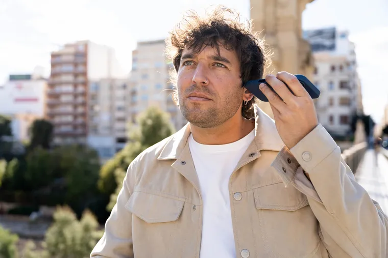 A man outdoors holding a phone to his ear trying to hear a weak call