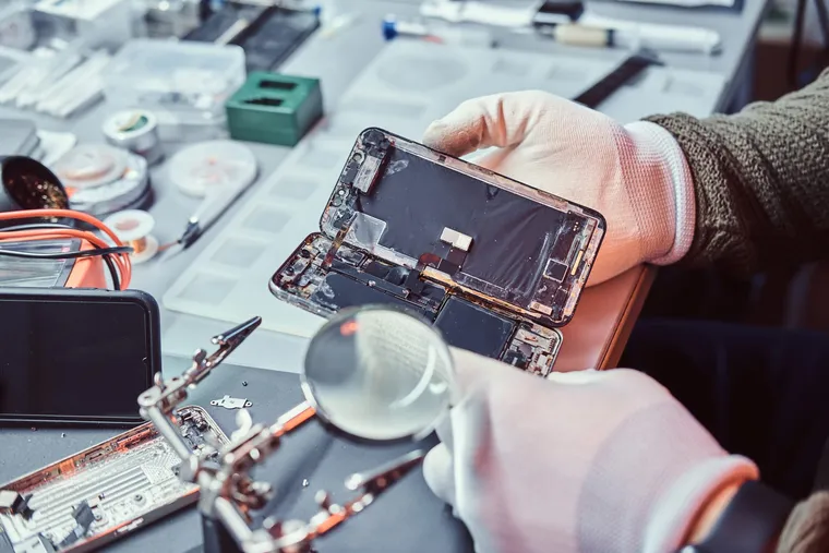 A technician inspecting a corroded phone board under a magnifier